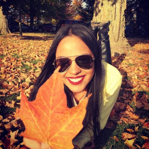Brazilian au pair Mariana wearing sunglasses and an autumnal jacket, surrounded by brown maple leaves.
