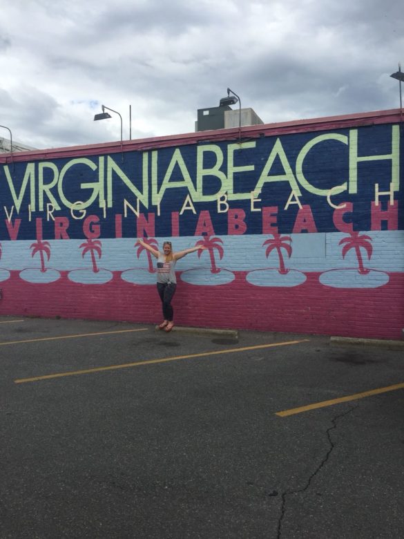 Merle posing in front of a colourful wall that says "Virginia Beach"